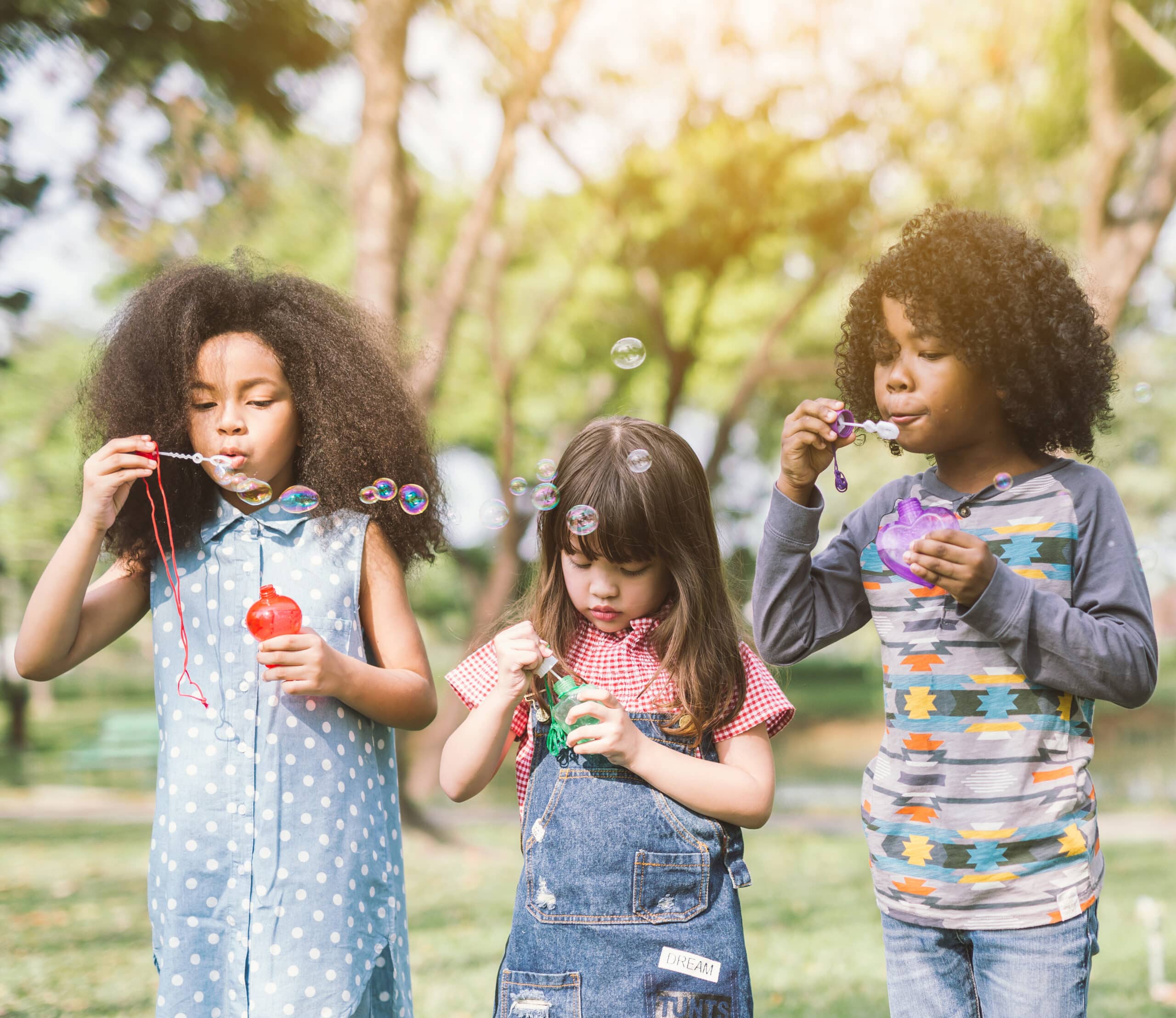Group of kids having bubble fun on green lawn in park